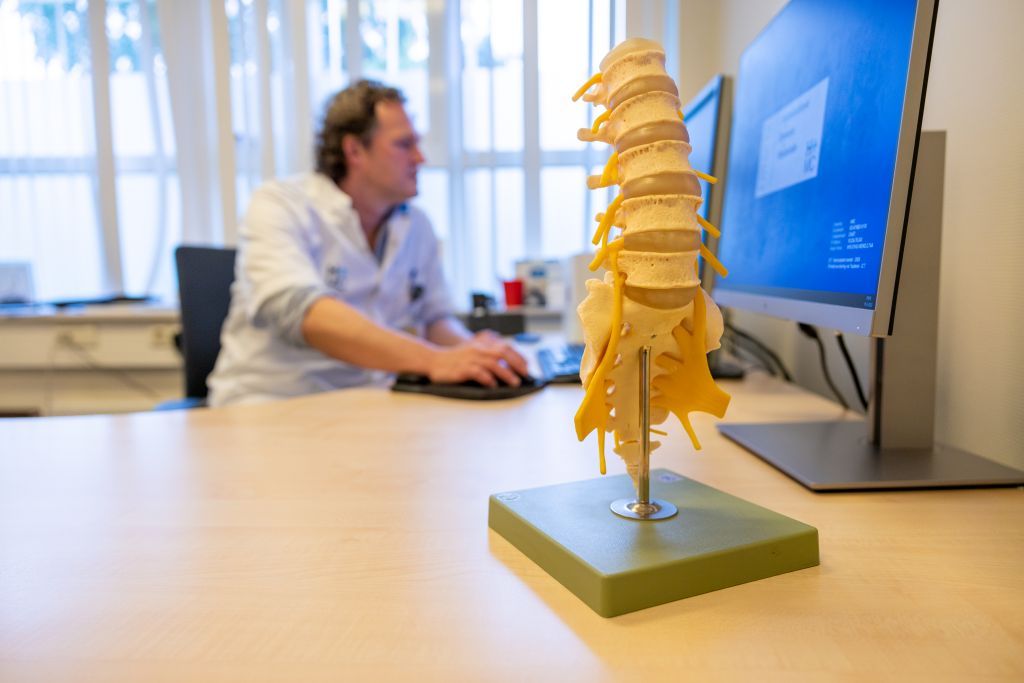 HMC neurochirurg Godard de Ruiter achter de computer, met voorbeeld van stuk ruggenmerg op de voorgrond