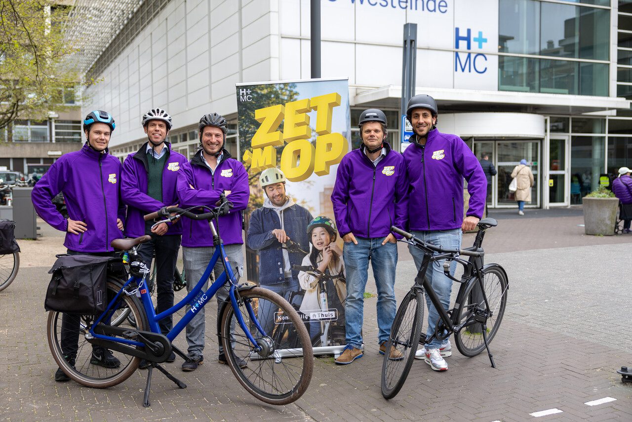 Artsen poseren voor het ziekenhuis met een fietshelm op hun hoofd. Zij vragen aandacht voor veilig fietsen.